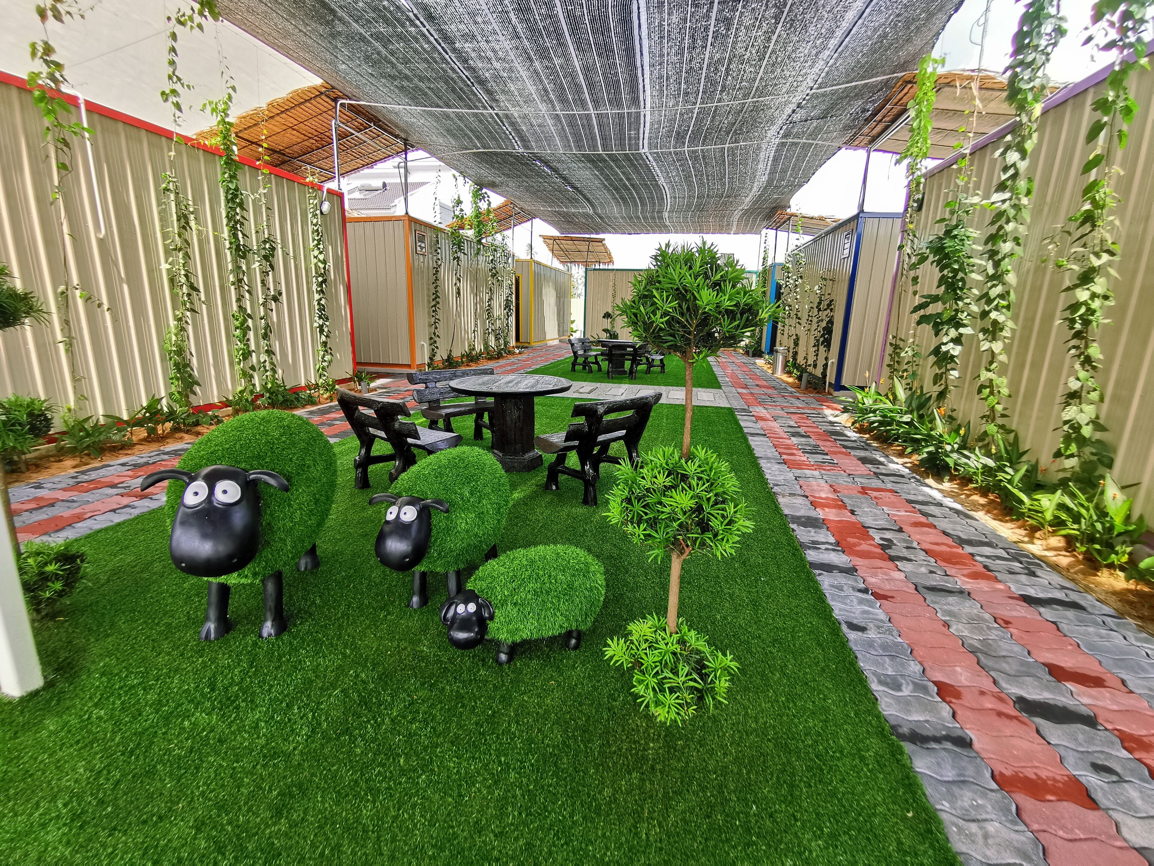 Un patio con césped artificial, una mesa y sillas, y figuras decorativas de ovejas.