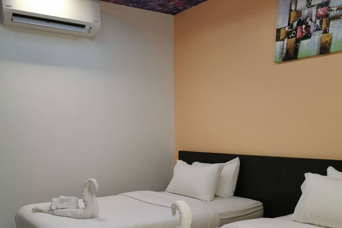 A hotel room with two beds, each with a swan-shaped towel, white bedding, and a black headboard.
