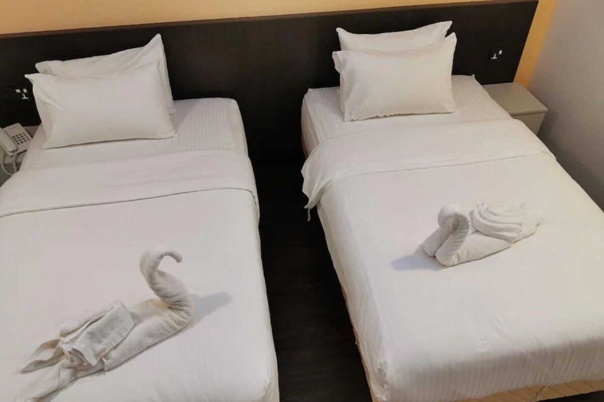 Dos camas individuales con ropa blanca, cabeceros, mesitas de noche y un teléfono sobre una cama.