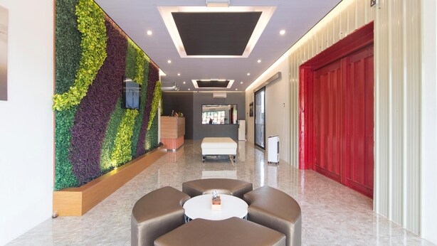 A modern lobby with a green vertical garden, a reception desk, a seating area with a round table, and a red door. - TT Dorf Hotel Matang (Taiping)