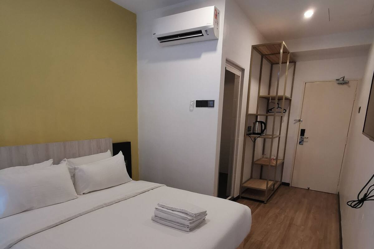 A hotel room with a bed, an air conditioning unit, a door, and a wooden floor.
