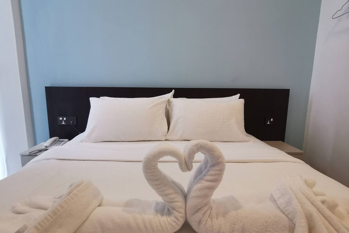A hotel room with a bed, pillows, a phone, and towels arranged in a heart shape.