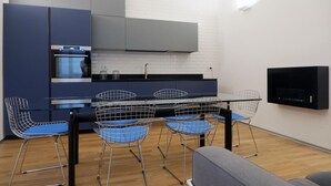 A modern kitchen with a dining area, featuring a black countertop, blue chairs, and a built-in TV. - Magdahause (Taranto)