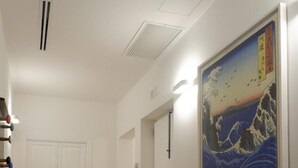 A hallway with a wooden floor, a bench, and a large painting of a wave on the wall. - Magdahause (Taranto)