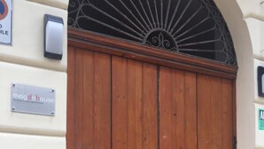 A large wooden double door with a metal decorative arch above it. - Magdahause (Taranto)