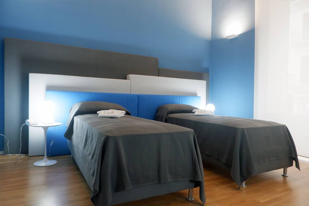 Quarto de hotel com duas camas, uma mesa de cabeceira e um criado-mudo.