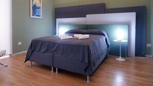 A modern bedroom with a large bed, a headboard, and a bedside table with a lamp. - Magdahause (Taranto)