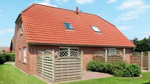Ein zweistöckiges Backsteinhäuschen mit rotem Ziegeldach, einem kleinen Fenster und einem Holztor.