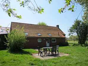 Situated in a serene rural setting, this charming house features a sloped roof with two skylights, a well-manicured lawn, and a cozy garden area with a table and chairs.