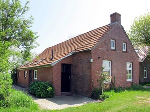 Traditional brick house with a sloped roof and chimney, set amidst a well-manicured lawn and paved driveway.