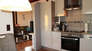 Eine moderne Küche mit Edelstahlgeräten, ein Essbereich mit Glastisch und ein Wohnzimmer mit Sofa und dekorativen Kissen.