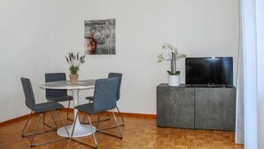 A modern living room with a dining table, chairs, a flat-screen TV, and a grey cabinet. - Junior Suite by Interhome (Ascona)