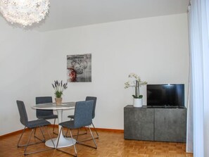 Una sala de estar moderna con una mesa de comedor, sillas, un televisor de pantalla plana y un mueble gris.