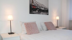 A bedroom with a bed, two bedside tables, two lamps, and a wall-mounted picture. - Junior Suite by Interhome (Ascona)