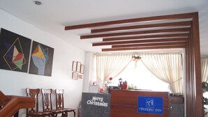 Un área de recepción con un mostrador de madera, una zona de estar con sillas y arte abstracto en la pared.