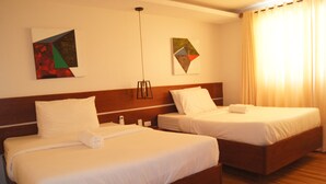 Habitación de hotel con dos camas individuales, cabecero de madera, lámpara de pared y dos cuadros abstractos.