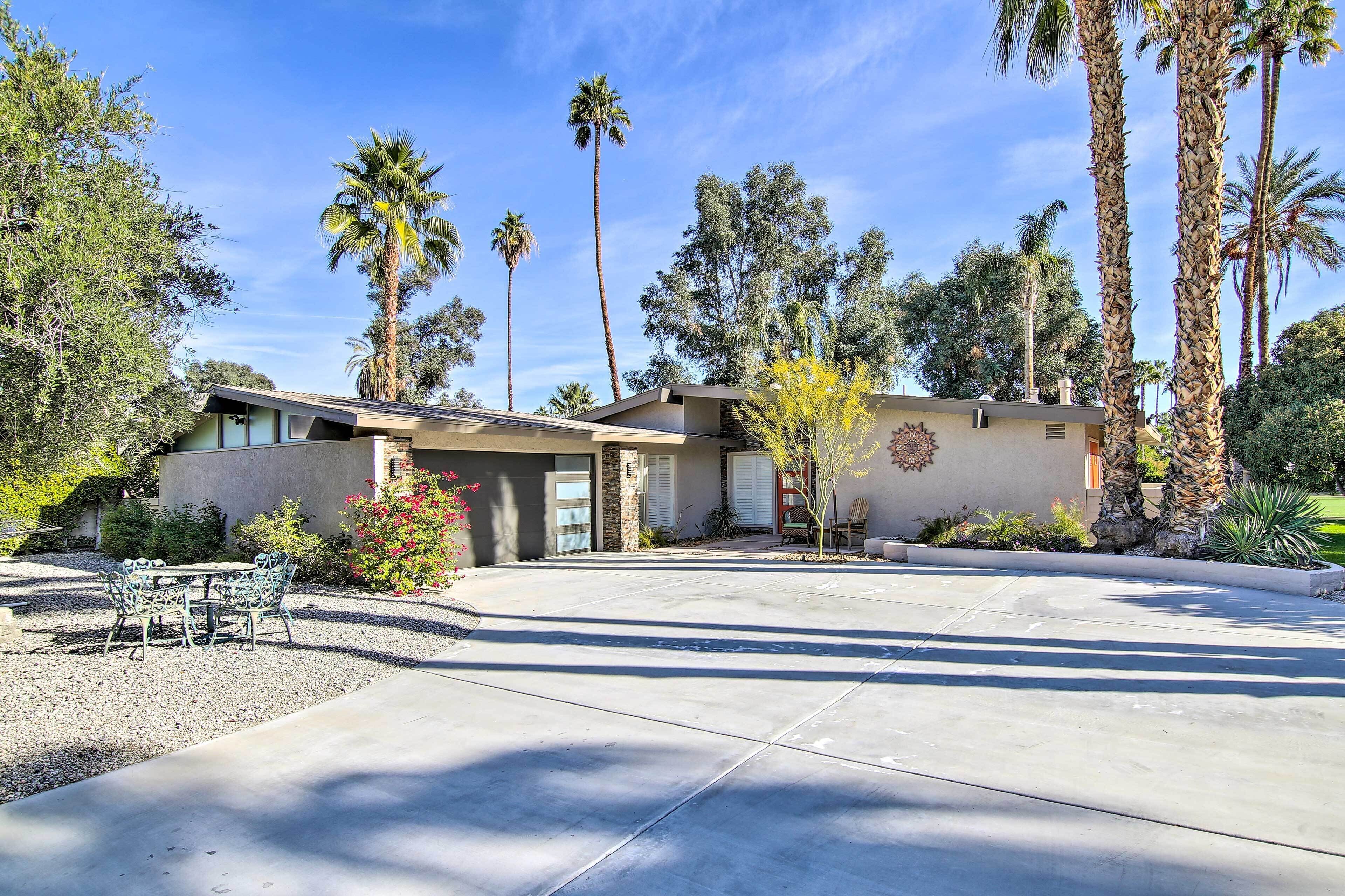 A modern house with a patio, palm trees, and a clear sky.