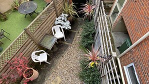 A narrow courtyard with a brick wall, a metal gate, and a small garden area with potted plants and a white chair. - 19 Station Road (Henley-on-Thames)