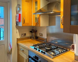 A kitchen with wooden cabinets, a stainless steel range hood, a gas stove, and a built-in oven. - 19 Station Road (Henley-on-Thames)