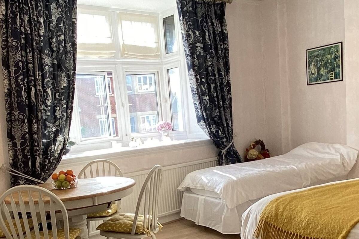 A room with a bed, a small table with chairs, and a window with curtains.