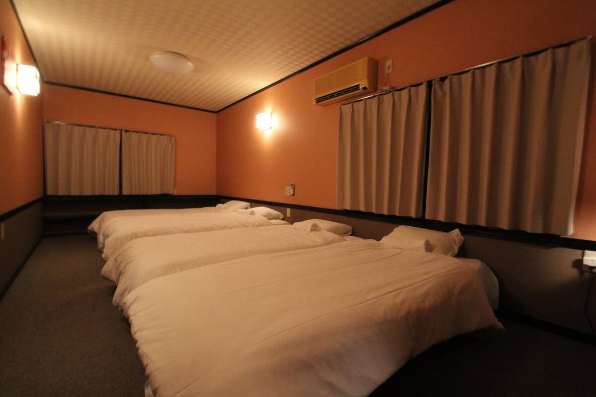 Habitación de hotel con dos camas, ventilador de techo, unidad de aire acondicionado y ventana con cortinas.