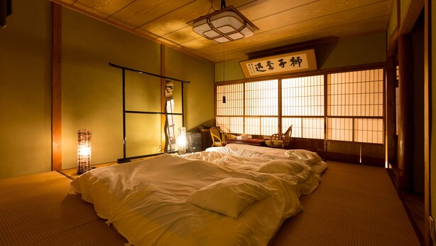 Une pièce de style japonais traditionnel, avec un sol recouvert de tatamis, un futon servant de lit, un paravent shoji et une lanterne suspendue.
