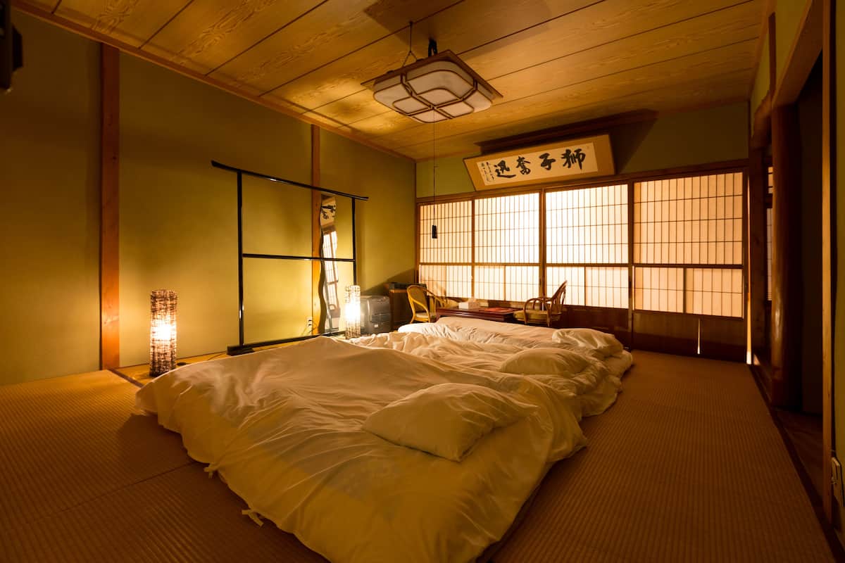 Una habitación tradicional japonesa con suelo de tatami, futón, pantalla shoji y una linterna colgante.
