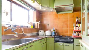 Une cuisine avec des meubles de couleur verte, un évier, une cuisinière et une fenêtre avec des rideaux.