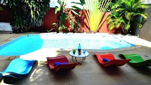 A swimming pool with colorful lounge chairs and a small table with bottles. - Sous le Badamier (pointe aux canonniers)