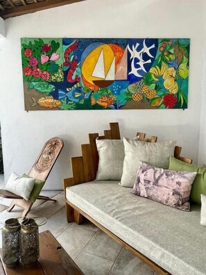 A room with a sofa, pillows, a wooden chair, and a large abstract painting on the wall. - Sous le Badamier (pointe aux canonniers)