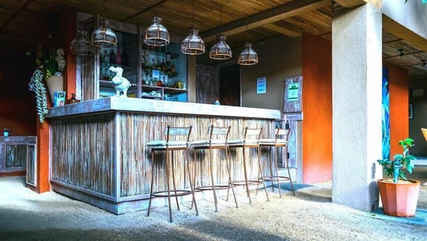 A bar area with a wooden counter, metal hanging lights, and bar stools. - Sous le Badamier (pointe aux canonniers)