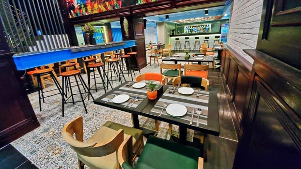 A restaurant with a bar area, multiple dining tables with chairs, and a colorful mural on the wall. - Sanctuary Hotel Yangon (Yangon)
