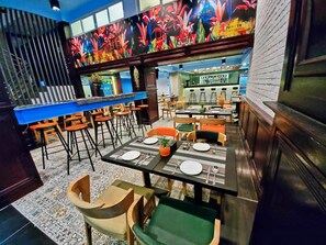 A restaurant with a bar area, multiple dining tables with chairs, and a colorful mural on the wall. - Sanctuary Hotel Yangon (Yangon)