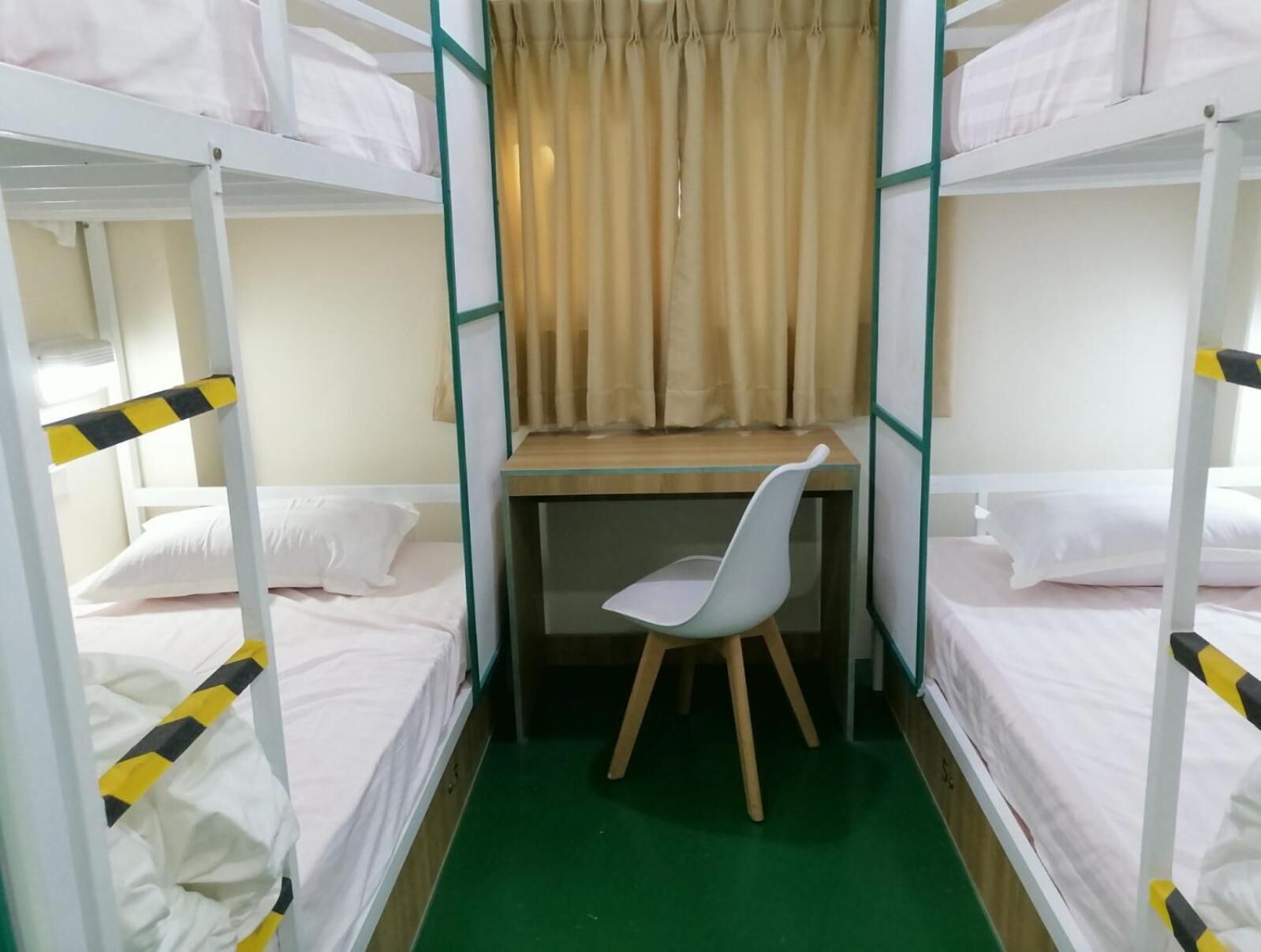Une chambre de dortoir avec des lits superposés, un bureau, une chaise et un rideau.