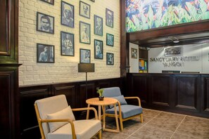 A reception area with framed portraits on the wall, a reception desk, and two chairs with a small table in the center. - Sanctuary Hotel Yangon (Yangon)