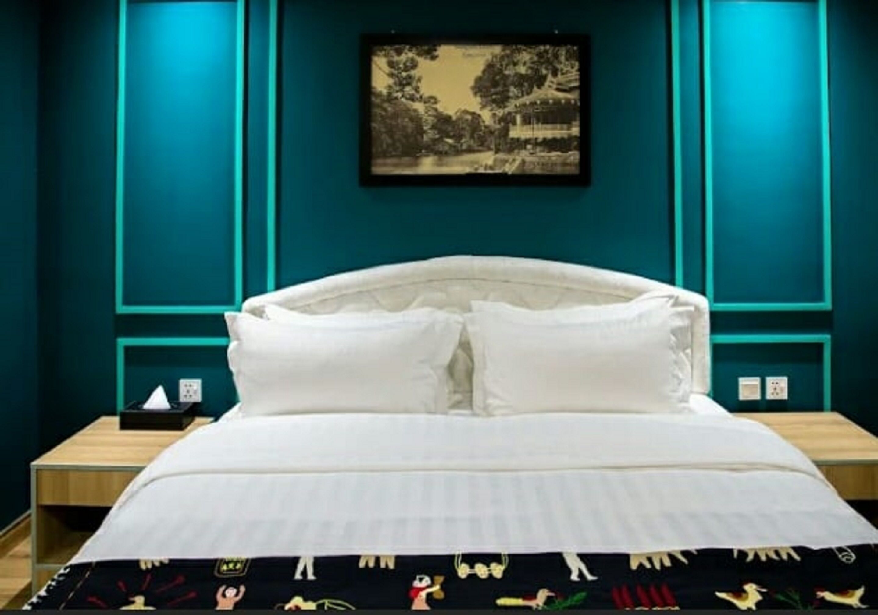 A neatly made bed with white linens and a black pillowcase with colorful patterns. There is a framed picture on the wall above the bed.