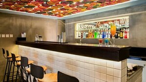 A bar area with a tiled wall, stools, and a bar counter with various bottles and glasses. - Sanctuary Hotel Yangon (Yangon)