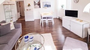 Una sala de estar moderna con sofá, mesa de centro y mueble para televisor. Hay una zona de comedor con mesa y sillas.