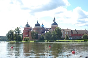 A historic building with domed architecture by a lake, surrounded by trees and a clear sky.