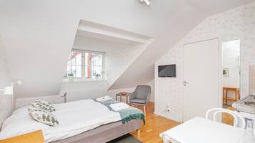 A bedroom with a bed, a desk, a chair, a TV, and a window.