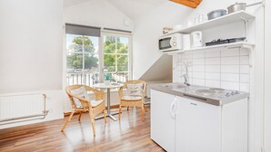 Una cocina moderna con armarios blancos, un microondas integrado y una estufa a gas. Hay un comedor con sillas de mimbre y una pequeña mesa redonda.
