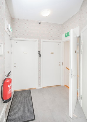 A hotel lobby with two white doors, a fire extinguisher, a green exit sign, and a ceiling light.