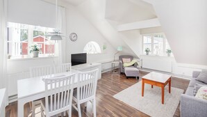 Un amplio apartamento tipo loft con comedor, sala de estar con sofá y mesa de centro, y un ventanal con vista a un edificio rojo.