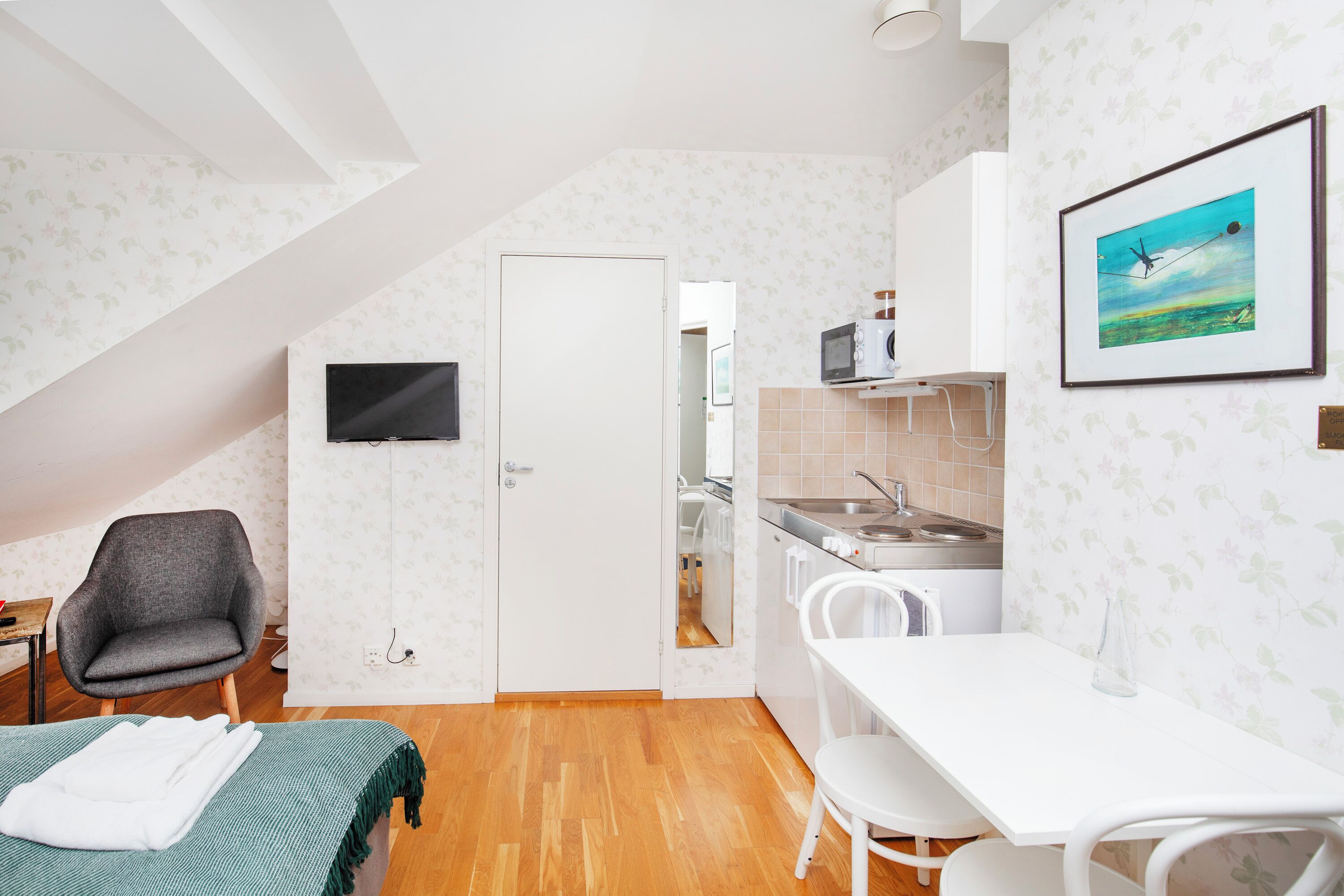 A compact kitchen with a dining area, a TV mounted on the wall, and a door leading to another room.