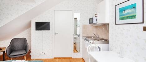 A compact kitchen with a dining area, a TV mounted on the wall, and a door leading to another room.
