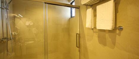 Ducha con paredes de vidrio, barra de apoyo, toallero con toallas dobladas y una pequeña ventana sobre la ducha.