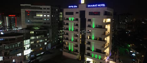 A hotel with multiple floors, illuminated by green lights, and a sign indicating it is the Da'amat Hotel.