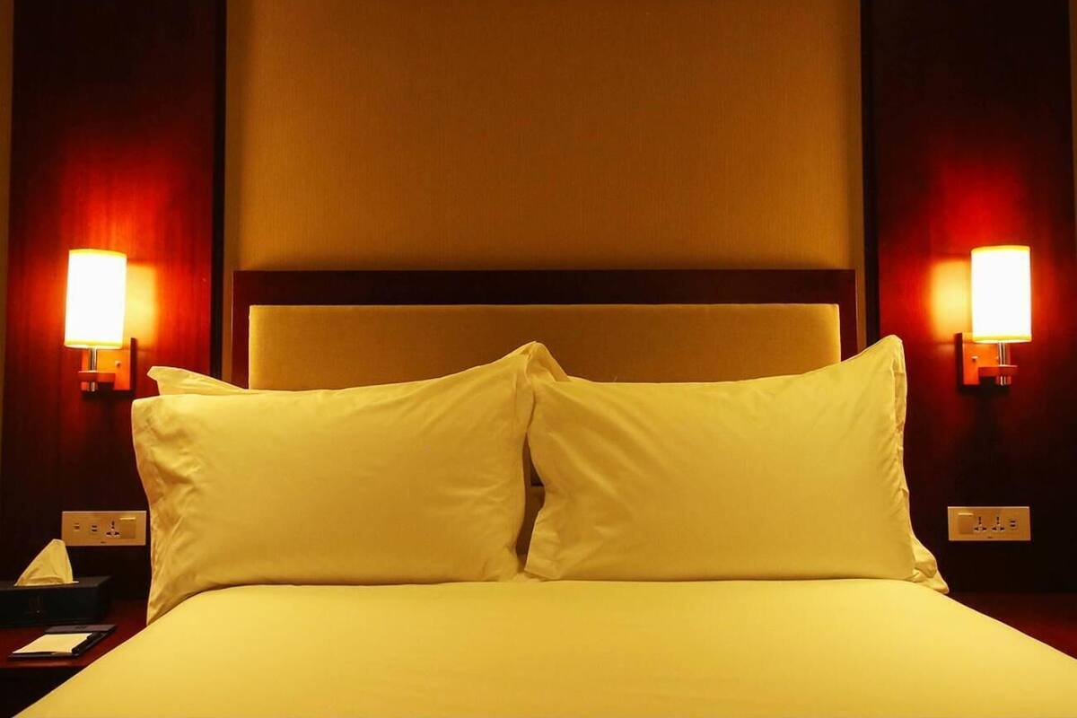 A hotel room with a bed, two bedside lamps, and a nightstand with a phone and a tissue box.
