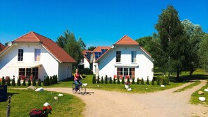 Rivi valkoisia taloja, joissa on punaiset katot, pyöräilijä pyörätiellä ja kirkas, sininen taivas.