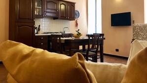 Una sala de estar acogedora con un sofá y un comedor con una mesa y sillas. Se observa una cocina con armarios de madera y una estufa.